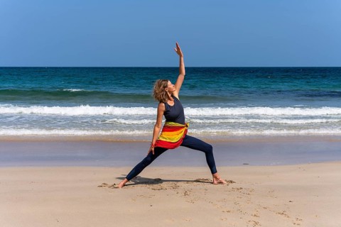 A woman doing yoga on a sandy beach by the sea. Shanti Virabhadrasana or Peaceful Warrior. Treen