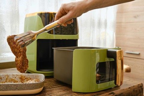 A hand lifts a piece of marinated meat and place it an air fryer, showcasing the cooking process.
