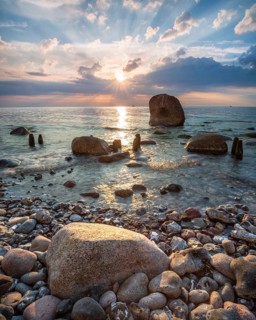 Sunrise on the shore of the Baltic Sea, boulders and old groynes in the water, Jasmund National