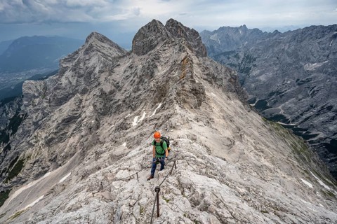 Mountaineer with helmet climbing in a secured climb on the rock, on a narrow rocky ridge, crossing
