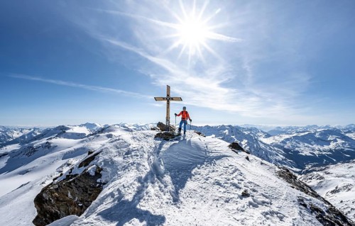 Ski tourer at the summit of Monte Cevedale with summit cross, sun star, mountain panorama,