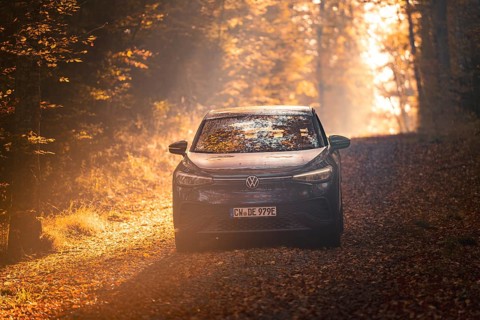 Car driving on a forest path covered with leaves on a sunny autumn day, electric car VW ID5,