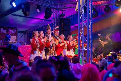 A group on stage at a carnival event, surrounded by a celebrating crowd, Fasching, Schlagerkuchen