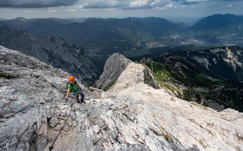 Mountaineer with helmet climbing on the rock in a secured climb, on a narrow rocky ridge, in steep