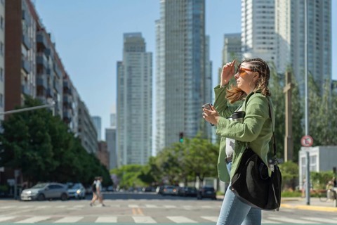 Young businesswoman crossing the street holding a coffee and protecting herself from the sun in