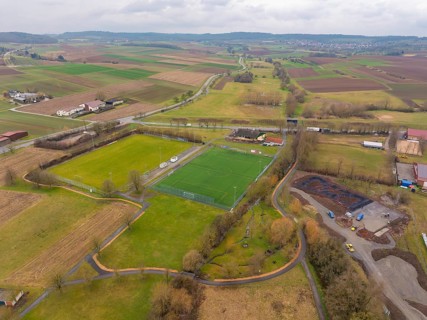 Green sports field surrounded by fields and scattered trees in a rural setting, Großbottwar,
