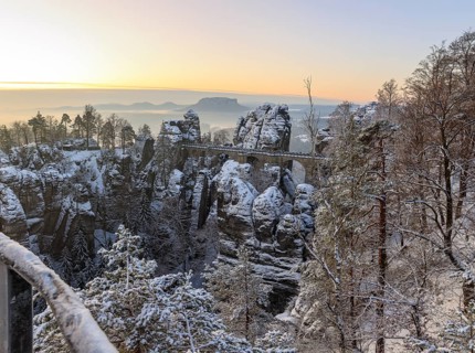 Snow-covered rock castle Neurathen and Bastei bridge in the morning, in the background the