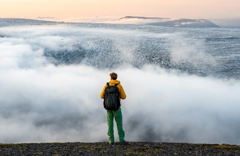 Young man in front of impressive landscape at sunset, fog, clouds moving around, glacier ice of the