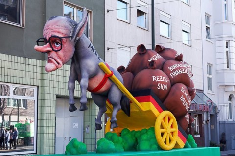 Chancellor candidate Friedrich Merz as a donkey figure in front of a cart with heavy sacks, debt