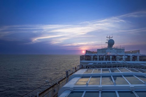 Cruise docked near scenic ocean beach landscape on a cruise vacation at sunset.
