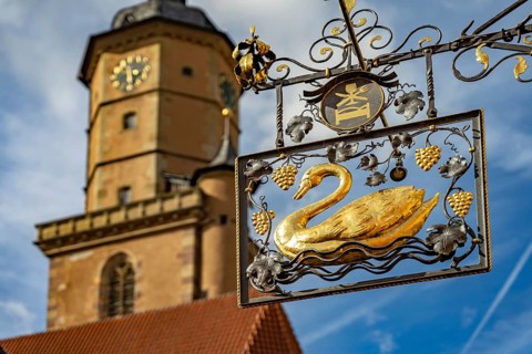 Golden sign Hotel Zur Schwane and the church tower of St Bartholomew in Volkach, Lower Franconia,