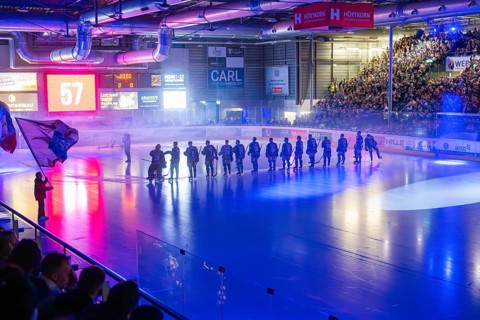 Ice hockey game with teams on the ice and fans watching in a brightly lit stadium, Heilbronner
