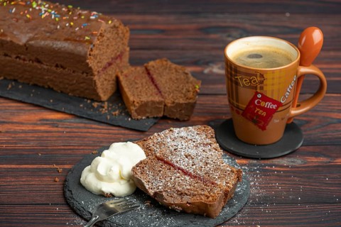 Chocolate cake, pieces with icing sugar and whipped cream, next to a cup of coffee