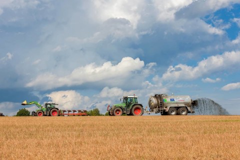 Two tractors in a field with a fertiliser spreader under a cloudy sky, Baden-Württemberg, Germany,