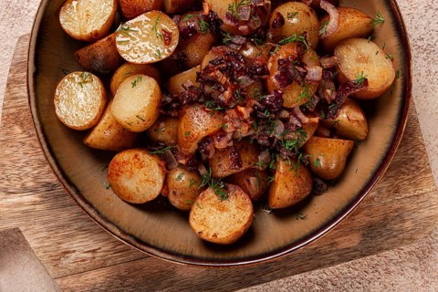 Golden roasted potatoes are served in a rustic bowl, topped with sweet caramelized onions and