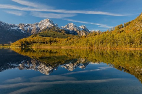 Lake Almsee in autumn with mountains reflected in the lake. Blue sky