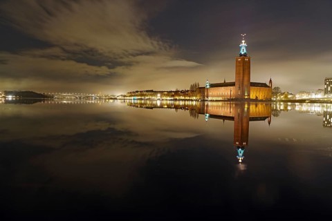 Night shot of an illuminated city building on the shore with reflection in the water, winter, ice,