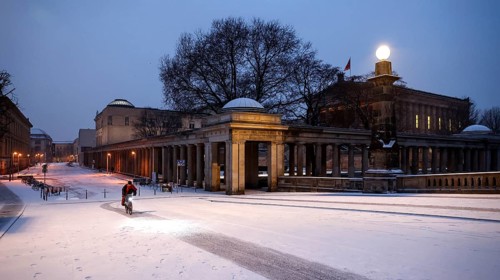 A cyclist rides over snow-covered streets at the old National Gallery in the early morning, Berlin,