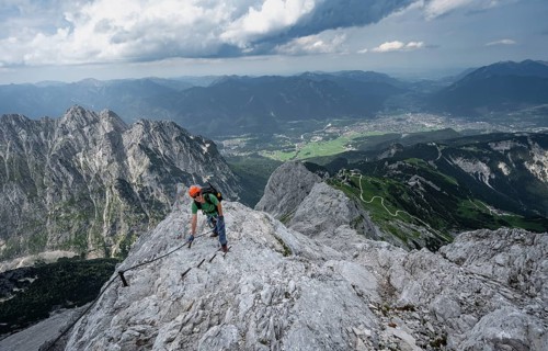 Mountaineer with helmet climbing on the rock in a secured climb, on a narrow rocky ridge, in steep