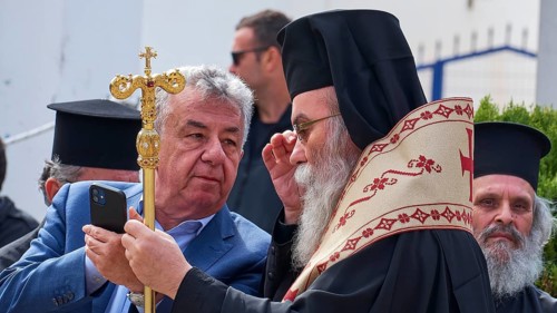 Archbishop Amphilochios, priest in religious dress looks at a smartphone during an outdoor