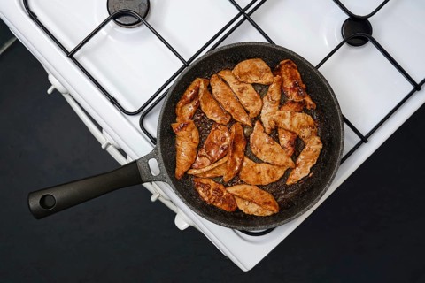 Juicy marinated pork strips sizzle in a frying pan, showcasing their golden brown color while being
