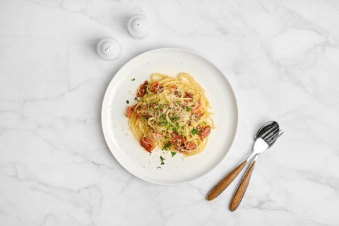 Overhead view of spaghetti carbonara sprinkled with cheese on a marble table. Salt shakers are