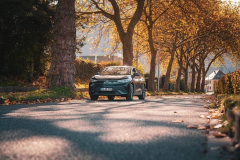 A Volkswagen drives through a tree-lined street in autumn in soft sunlight, electric car VW ID5,
