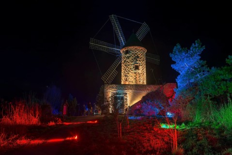 Stone windmill at night in a landscape illuminated with red and blue lights, world of lights,