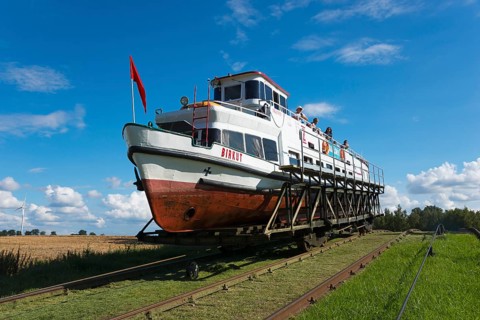 A boat on a hoist being transported over rails, under a clear summer sky, Upland Canal,