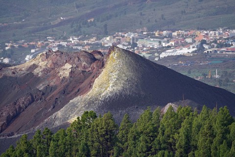 Volcanic ash cone above a cityscape, surrounded by green vegetation, last volcanic eruption of