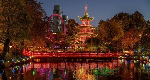 Illuminated pagoda, colourful lighting, roller coaster, trees, cityscape at night with modern