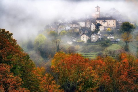 Village view of Corippo in the fog surrounded by autumn-coloured deciduous trees, Verzasca Valley,