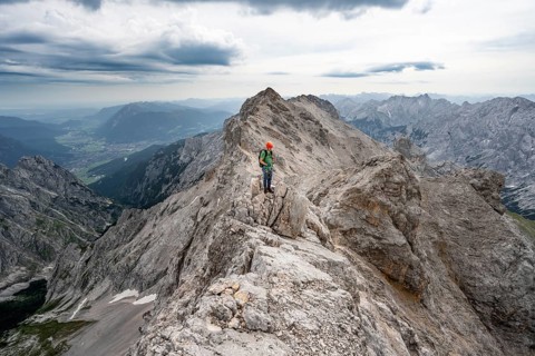 Mountaineer with helmet on a narrow rocky ridge at sunrise, crossing the Jubiläumsgrat, view of