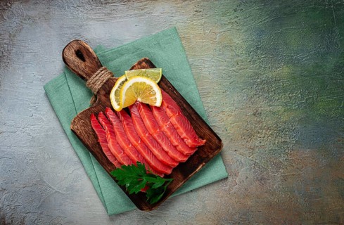 Chum salmon, cold smoked, sliced, on a cutting board, with lemon and parsley, top view, close-up,