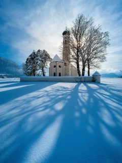 The pilgrimage church of St Coloman in a snow-covered landscape in winter backlit, Schwangau,
