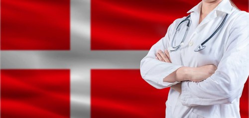 Doctor With Crossed Arms On Denmark Flag. Denmark Health And Care Concept. Female Doctor On Denmark