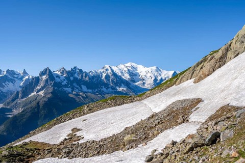 Snow fields and hiking trail in front of mountain panorama, view of glaciated mountain peak Mont