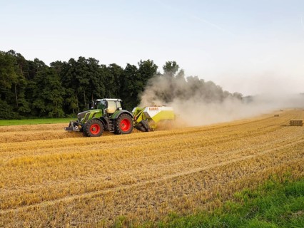Farmer baling straw with his tractor and baler on a field after the corn harvest, the air above the