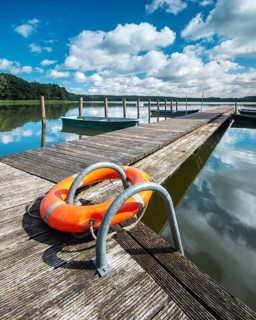 Jetty with rowing boats at Moderfitzsee under a blue sky with cumulus clouds in summer, in front a