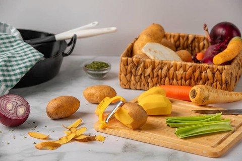 Peeled potatoes on a wooden board next to soup vegetables, preparation for cooking