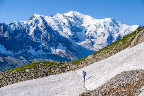 Mountaineer crossing a snowfield, view of spectacular glaciated peaks of Mont Blanc, Mont Blanc