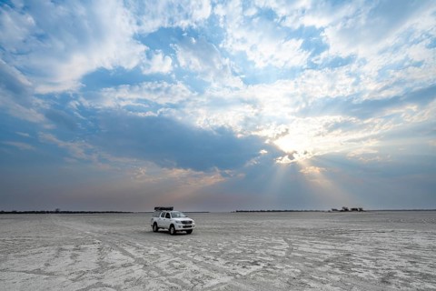 Toyota Hilux off-road vehicle on a salt pan, dramatic clouds with sunbeams, wide open plain, Nxai