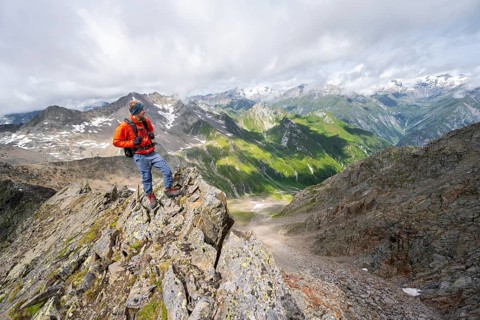Mountaineer on a steep rocky ridge, at the summit of Lasörling, view of mountains of the Venediger