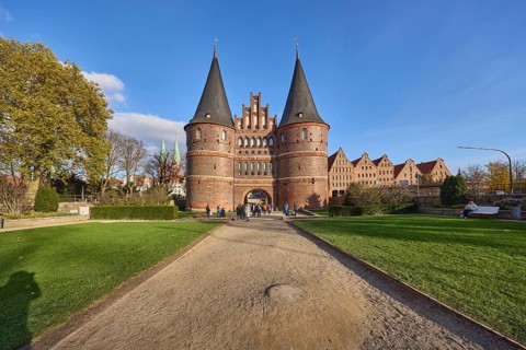 City gate, historic brick building, footpath made of sand, garden with lawn, trees, blue sky with