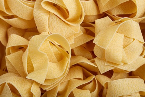 Raw pappardelle pasta, pasta nests, in a paper box, top view, no people