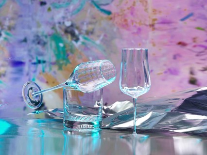 Various glasses on silver foil, behind them various splashes of colour, studio shot