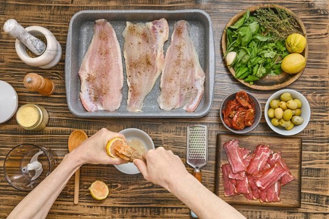 Hands squeeze lemon juice to prepare a marinade for fish fillets arranged in a baking tray