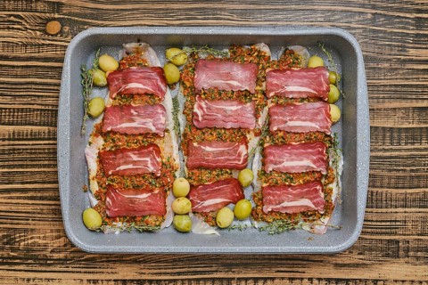 A beautifully arranged dish of thinly sliced meat is placed on a baking tray. The meat is topped