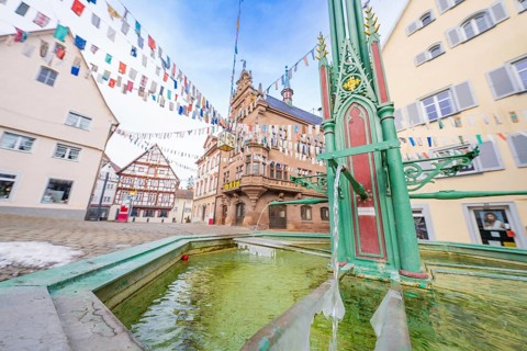 Historic fountain in an old town with colourful pennants and surrounding architecture, Wend