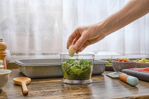 A person is adding a clove of garlic to a bowl filled with fresh greens, highlighting the process